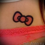 Фото тату головы Hello Kitty на задней части шеи девушки. Маленький и милый рисунок татуировки в ярких цветах.