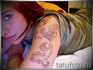 Фото тату: рисунок хной на плече девушки, выполненный в коричневых тонах. Эскиз татуировки состоит из растительных элементов и узоров.