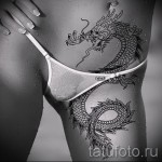 Фото тату дракона на бедре, выполненного в черно-белых тонах. Изображение демонстрирует детализированную проработку, плавные линии и элегантный стиль.