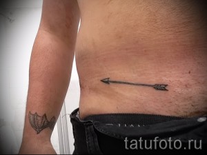 Фото татуировки: стрела на боку и летучая мышь на предплечье. Простые, графичные рисунки.
