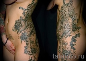 Фото тату: Черно-серая татуировка на боку, изображающая тигра, обвитого цветами. Детализированный рисунок татуировки с плавными линиями и реалистичными деталями.