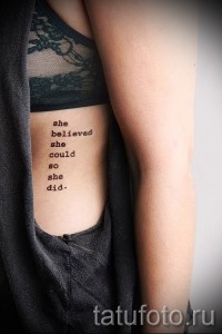Фото тату надписи 'she believed she could so she did' на боку. Черная, минималистичная татуировка, вдохновляющая на достижение целей.