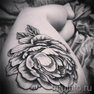 Фото тату пиона на бедре в черно-белом исполнении. Крупный цветок с детально проработанными лепестками и листьями.