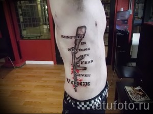 Фото тату на боку: стилизованная надпись 'RESPECT IS NOTHING BUT FEAR GIVEN VOICE' с изображением пистолета и брызгами краски.