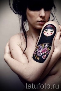Фото тату: матрешка с цветами на женском плече. Красивый и оригинальный рисунок татуировки в традиционном стиле.