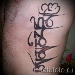 Фото тату: черная татуировка с именем "ZAVONE" и годом "2008" на мужском бедре, выполненная в стилизованном шрифте.
