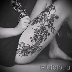 Фото тату: изящная татуировка с цветами и листьями, обвивающая бедро девушки. Черно-белое изображение.