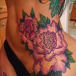 Фото тату с изображением пышных пионов на спине и шее. Красочный рисунок с использованием розовых, фиолетовых и зеленых оттенков.