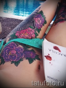 Фото тату с изображением пышных пионов на бедре. Красочный рисунок с использованием розовых и фиолетовых оттенков.