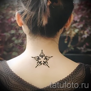 Фото тату: небольшой черный рисунок в виде острого символа на затылке девушки. Минималистичный дизайн, четкие линии, аккуратное исполнение.