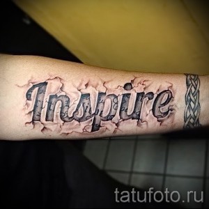 Фото тату надписи 'Inspire' на предплечье, выполненной в стиле 3D с эффектом разбитой кожи и трещин. Черно-серые тона.