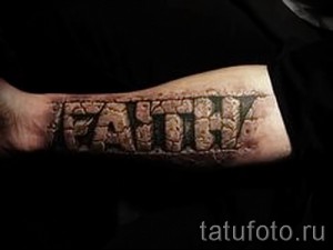 Фото тату надписи "DEATH" на предплечье, выполненной в мрачном стиле с эффектом разрушенного камня и черных оттенков.