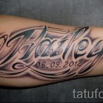 Фото тату на предплечье с именем "Hailey" и датой "06.09.2012", выполненной в черно-белом стиле с добавлением теней и узоров.