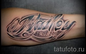 Фото тату на предплечье с именем "Hailey" и датой "06.09.2012", выполненной в черно-белом стиле с добавлением теней и узоров.