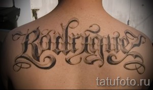 Фото тату надписи "Rodriguez" на спине, выполненной в готическом стиле с изящными завитушками и черными оттенками.