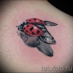 Фото тату: реалистичная красная божья коровка с черными точками на плече. Детализированные крылья и тени.