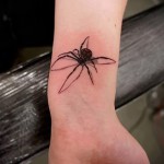 Фото маленькой татуировки паука на запястье. Простой, но элегантный рисунок черного паука с тонкими лапками. Идеально для любителей минимализма.