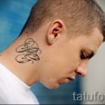 Фотография небольшой татуировки с буквой 'B', выполненной в черном цвете на шее мужчины. Стильный и лаконичный дизайн.