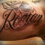 Фото татуировки с именем 'Roman' и изображением розы на плече. Черно-красный рисунок татуировки, выполненный в реалистичном стиле.