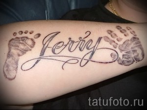 Фото тату с именем 'Jerry' и отпечатками детских ножек, выполненное на предплечье. Нежный дизайн и символическое значение делают эту татуировку особенной.