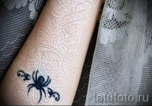 Фото тату: Белая татуировка в виде сложной мандалы с изображением черного паука. Оригинальный и мистический дизайн.