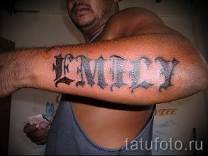 Фото тату с именем 'Emily', выполненное в готическом стиле на предплечье. Темные тона и острые углы придают татуировке мрачный и выразительный вид.