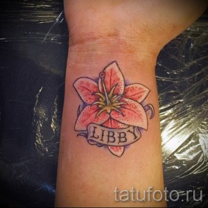 Фото тату с изображением цветка лилии и надписью 'LIBBY' на запястье. Нежный и женственный рисунок татуировки.