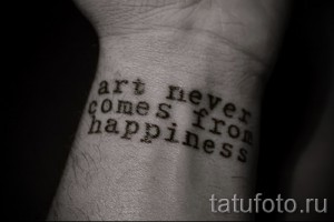 Фотография татуировки с цитатой "art never comes from happiness" на запястье руки. Рисунок выполнен в стиле леттеринг черным цветом.
