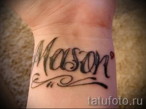 Фото татуировки с именем 'Mason' и маленьким сердечком на запястье. Черно-серый рисунок татуировки, выполненный в каллиграфическом стиле.