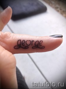 Фотография татуировки с именем 'George', выполненной изящным каллиграфическим шрифтом на пальце.