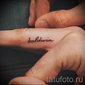 Фотография крошечной татуировки с надписью 'Baldwin', выполненной на фаланге пальца.