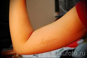 Фото тату надписи 'hope', выполненной белыми чернилами на предплечье, в каллиграфическом стиле.