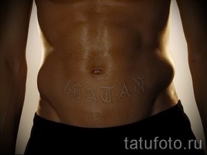Фотография белой татуировки на животе, изображающей имя "Zlatan". Имя выполнено стилизованным шрифтом в технике white ink.