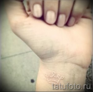 Фотография минималистичной белой татуировки на запястье, изображающей знак зодиака Лев с короной. Нежный рисунок татуировки выполнен в технике white ink.