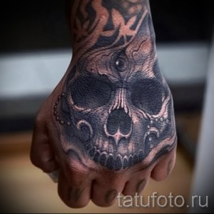 Черно-серый фото татуировки на руке: череп с четками и узорами. Детализированный рисунок, готический стиль, реалистичный дизайн.