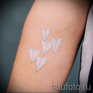 Фото тату с изображением нескольких бумажных самолетиков, выполненных в минималистичном стиле тонкими линиями на руке.