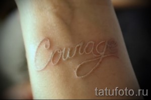 Фото тату: Белая надпись 'Courage' (Мужество) на запястье. Элегантный и минималистичный дизайн, символизирующий силу духа.