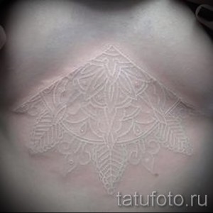 Фото белой татуировки в виде кружевной мандалы на груди. Детализированный узор, имитирующий кружево.