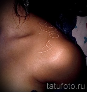 Фото минималистичной белой татуировки в виде абстрактного узора на плече. Тонкие линии и геометрические формы создают элегантный дизайн.