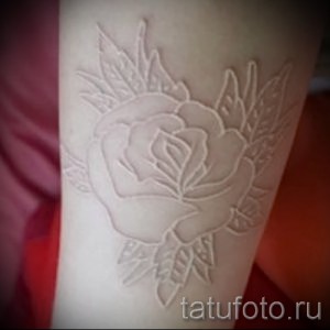 Фото тату белой розы на предплечье, выполненной в технике white ink. Детализированный рисунок с листьями и бутонами.