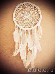 Фото тату: Белый ловец снов на коже. Детализированный рисунок с перьями и кружевной сеткой, выполненный в минималистичном стиле.
