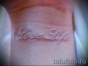 Фото белой татуировки с надписью "Love Life" на женском запястье. Простая и вдохновляющая надпись, выполненная белыми чернилами.