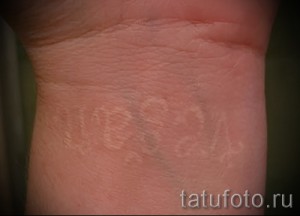 Фото белой татуировки с надписью на запястье. Нечеткая надпись, выполненная белыми чернилами, создает эффект таинственности.
