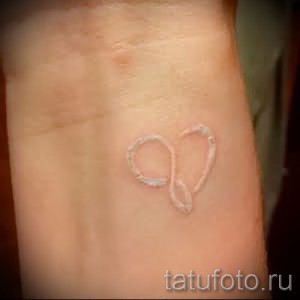 Фото белой татуировки в форме символа бесконечности на женском запястье. Минималистичный и элегантный рисунок.