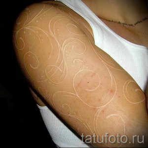 Фото тату: изящный белый растительный орнамент, покрывающий плечо, выполненный в технике white ink, с плавными линиями и витиеватыми узорами.