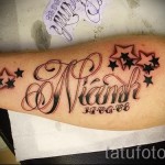 Фото татуировки с именем 'Niamh', датой '11.06.88' и черными звездами, выполненной на предплечье в красно-черной гамме.