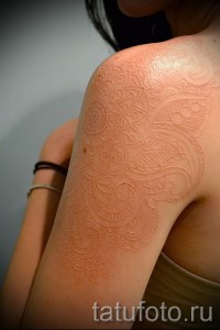 Фото белой татуировки: сложная мандала, выполненная на плече в технике white ink, создающая эффект тонкого, изящного рисунка.