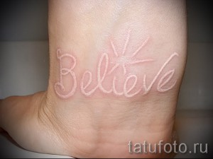 Фото белой татуировки на лодыжке: надпись 'Believe' выполненная каллиграфическим шрифтом. Нежный и вдохновляющий рисунок.