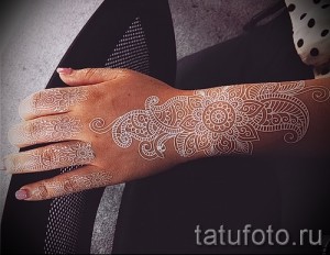 Фото белой татуировки в стиле хенд-мейд на руке девушки. Сложный узор из геометрических фигур и растительных элементов, выполненный белыми чернилами.