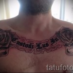 Фото тату с двумя розами и надписью 'Custodi Lus In' на груди. Черно-серые тона, детализированные цветы и лента с текстом.